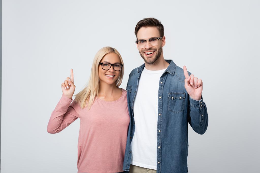 Χαμογελαστό ζευγάρι με γυαλιά που δείχνουν με τα δάχτυλα απομονωμένα στο γκρι - Φωτογραφία, εικόνα