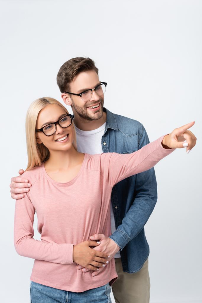 Smiling woman in eyeglasses pointing with finger near boyfriend isolated on grey - Photo, Image