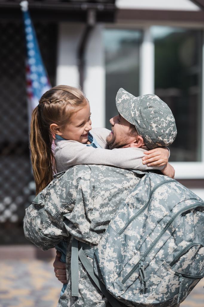 Glücklicher Vater in Militäruniform umarmt Tochter auf verschwommenem Hintergrund - Foto, Bild