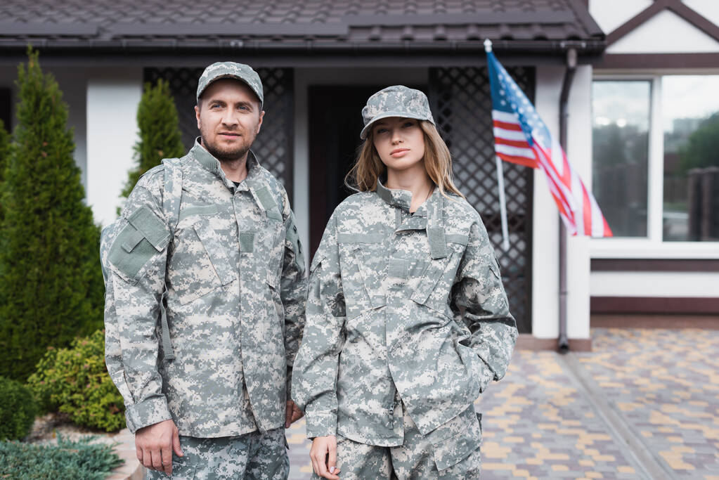 Military couple in uniforms standing together and looking at camera near house - Photo, Image