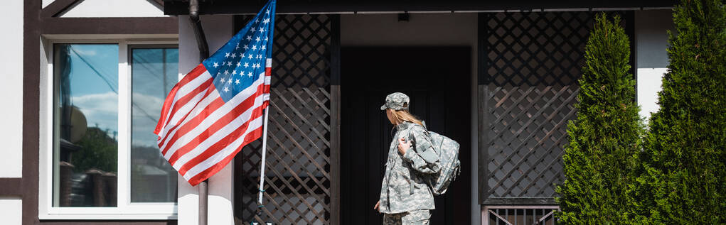 Военнослужащая с рюкзаком покидает дом, стоит на пороге, знамя - Фото, изображение