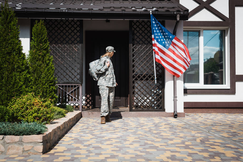 Military servicewoman with backpack leaving house, standing on threshold - Photo, Image