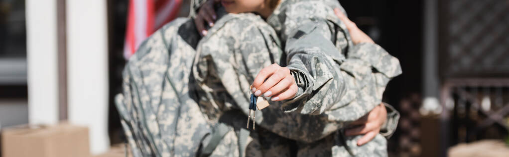 Vista recortada de las teclas con borrosa pareja militar abrazando en el fondo, bandera - Foto, imagen