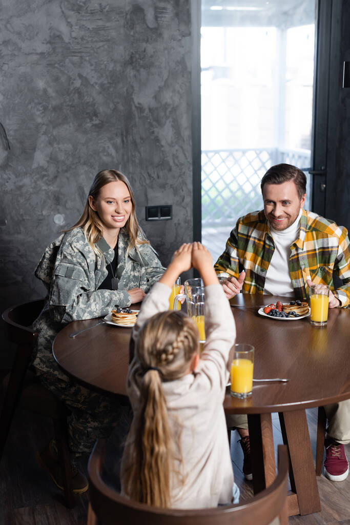 キッチンのテーブルに座っている間に、笑顔の夫婦と娘は朝食を持っています  - 写真・画像