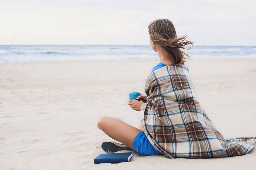 Mujer joven sentada en la playa y mirando al mar. Concepto de relajación - Foto, Imagen