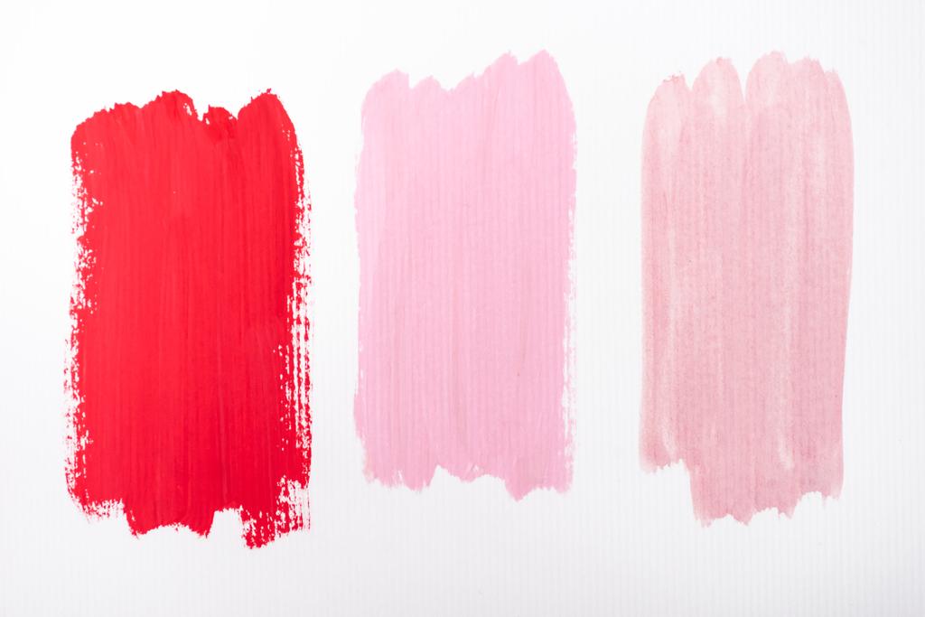 Draufsicht auf abstrakte rosa und rote Pinselstriche auf weißem Hintergrund - Foto, Bild