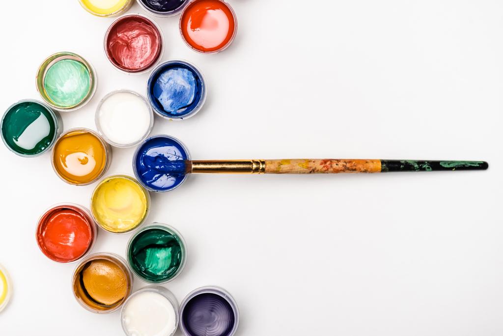 Beyaz arkaplanda Gouache boya ve boya fırçalarının üst görünümü - Fotoğraf, Görsel