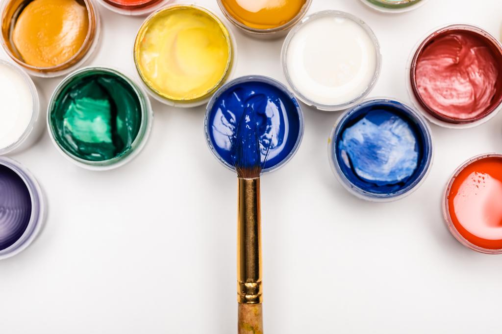 Beyaz arkaplanda renkli Gouache boyaları ve boya fırçalarının üst görünümü - Fotoğraf, Görsel