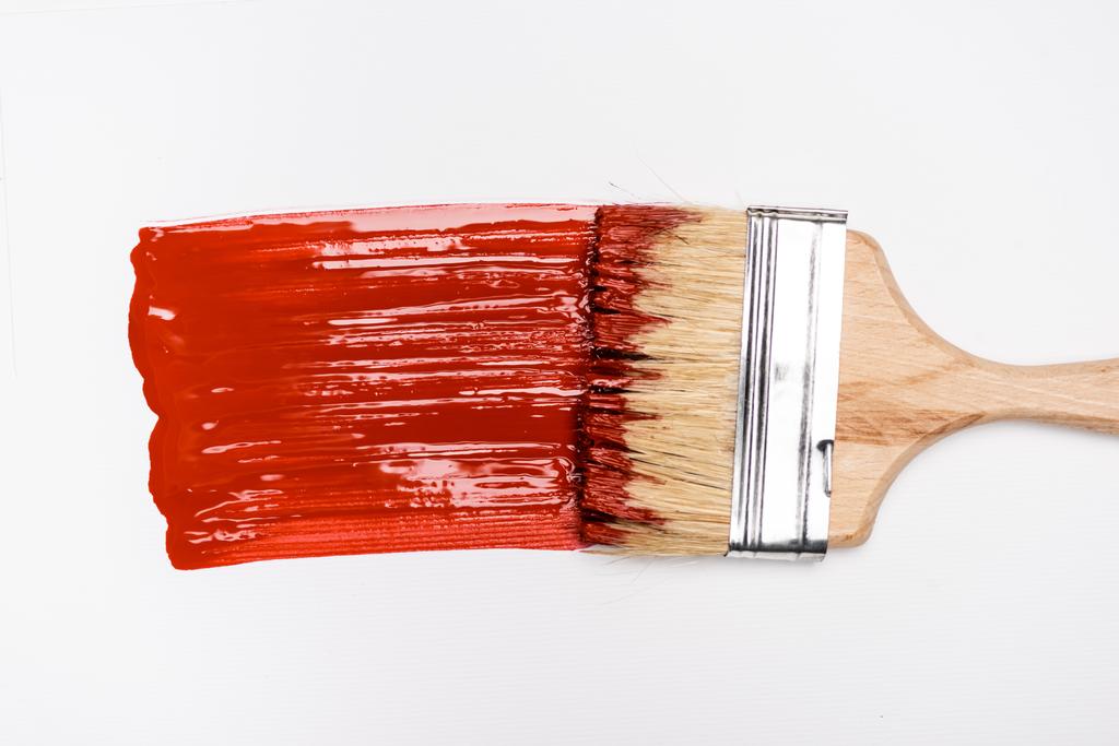 bovenaanzicht van penseel nabij kleurrijke rode verf penseelstreek op witte achtergrond - Foto, afbeelding