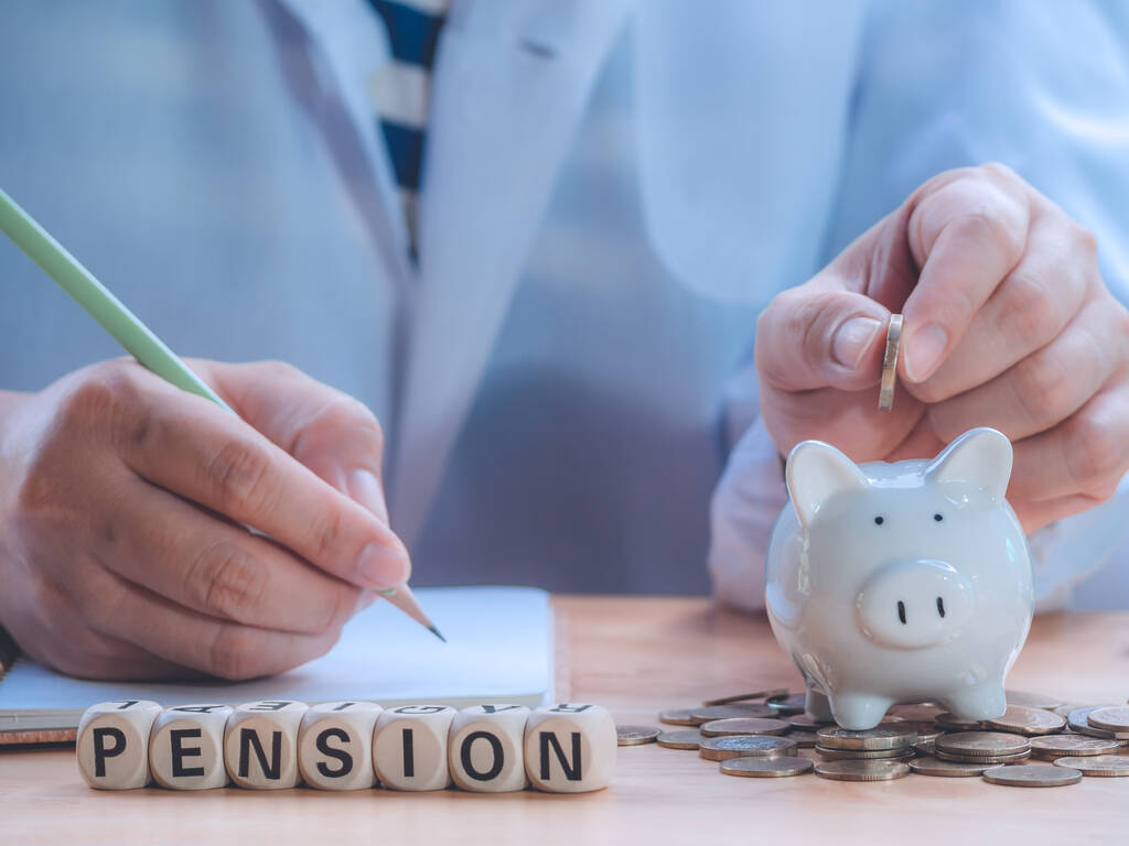 Closeup wooden block written PENSION against senior man hand putting coin into piggy bank to saving money and writing income expense for retirement financial and pension annuity insurance. - Photo, Image
