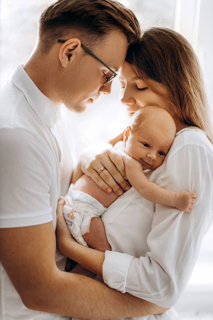 Родители с новорожденной девочкой, любящая мама держит маленькую дочку на руках, заботливый муж мягко обнимает обожаемую жену, улыбается, наслаждается нежными семейными моментами, прощаясь с понятием - Фото, изображение