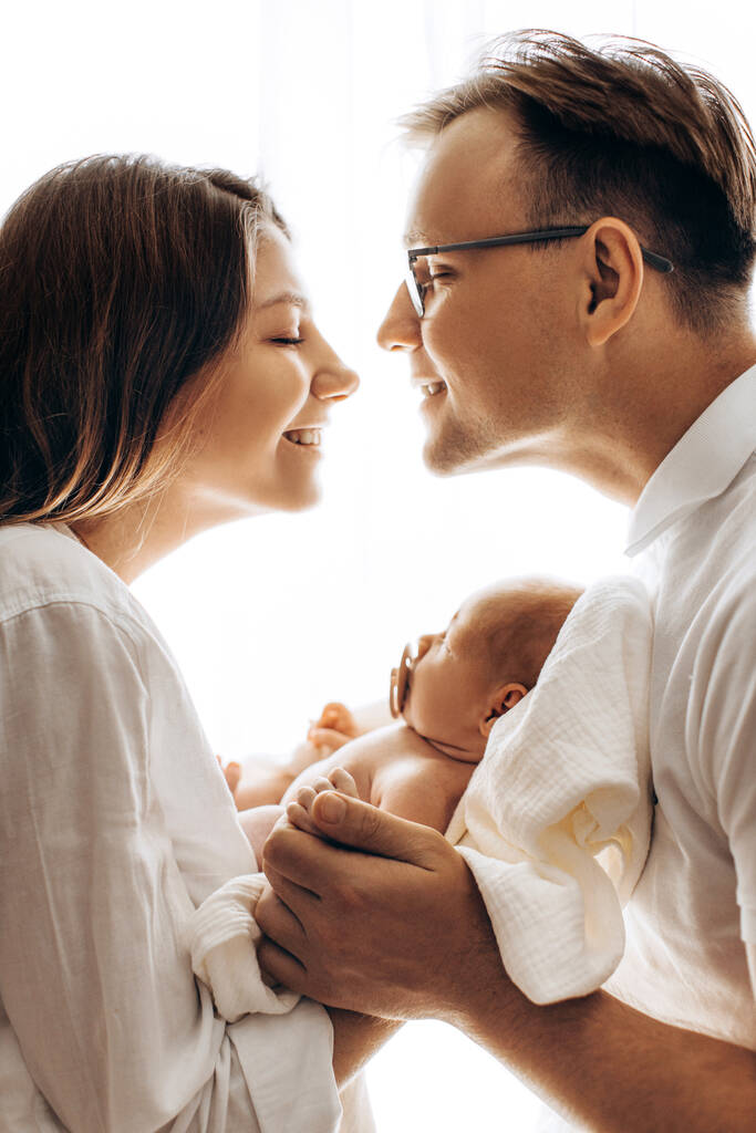 Boldog fiatal család kislánnyal, gyönyörű anya tart aranyos újszülött baba karokban, gondoskodó apa fogja a kezét imádnivaló kislány, anya és apa mosolyog, szülői koncepció - Fotó, kép