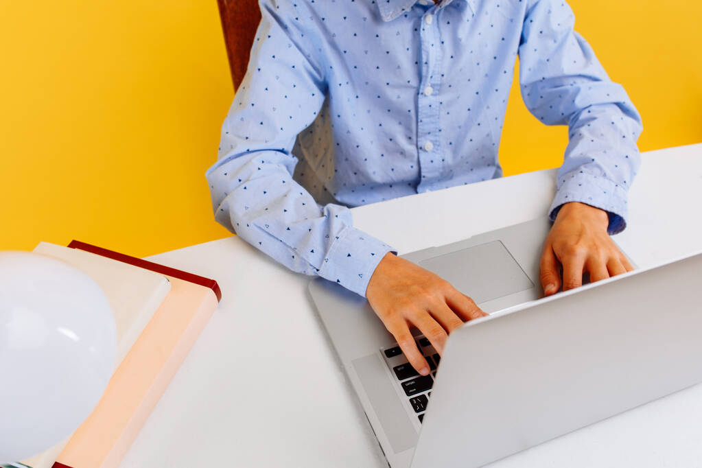 Школьник, обучающийся дома и выполняющий домашнюю работу с помощью ноутбука, на желтом фоне, дистанционное онлайн-обучение - Фото, изображение