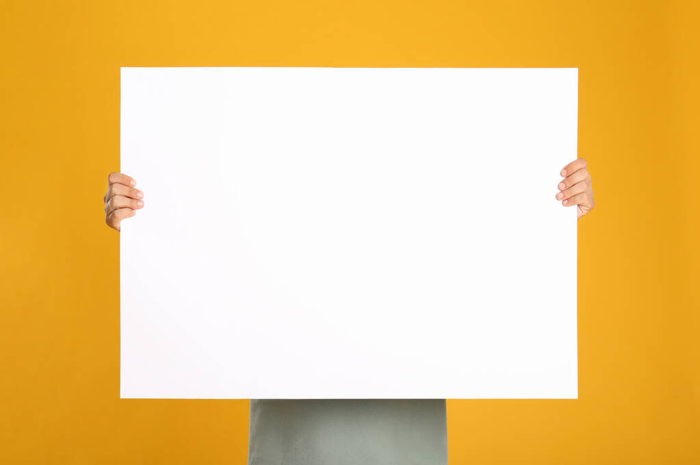Άντρας με λευκή λευκή λευκή αφίσα στο κίτρινο φόντο. Mockup για σχεδιασμό - Φωτογραφία, εικόνα