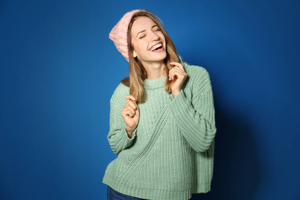 Mujer joven feliz con suéter cálido y sombrero de punto sobre fondo azul - Foto, imagen