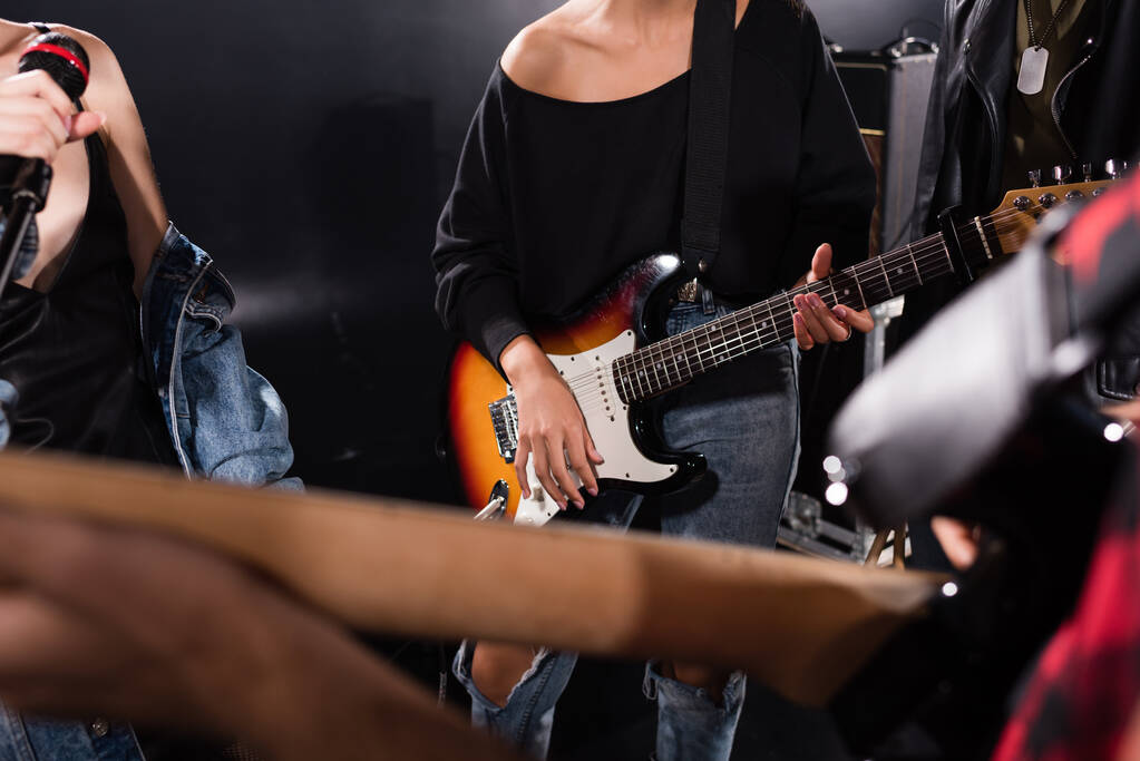 KYIV, UKRAINE - 25 СЕРПНЯ 2020: Покритий погляд на жінку з електричною гітарою біля жіночого вокалу з мікрофоном на розмитому передньому плані. - Фото, зображення
