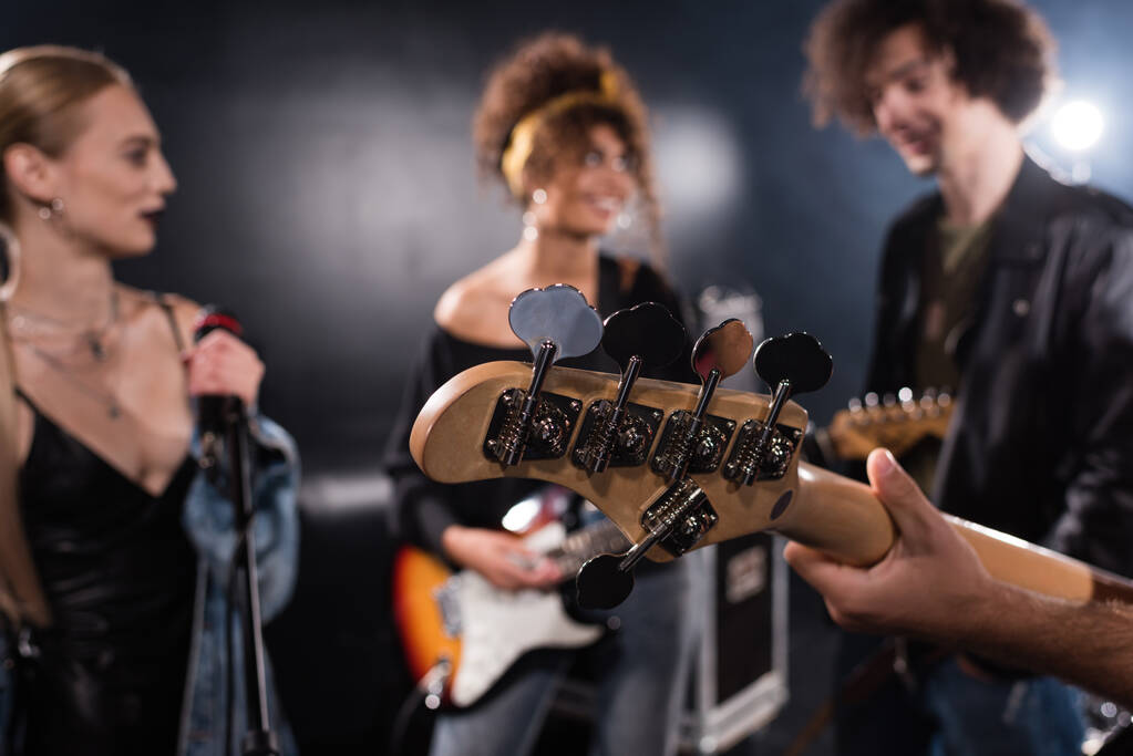 KYIV, UCRANIA - 25 de agosto de 2020: Músico sosteniendo la guitarra eléctrica con miembros borrosos de la banda de rock en el fondo - Foto, Imagen