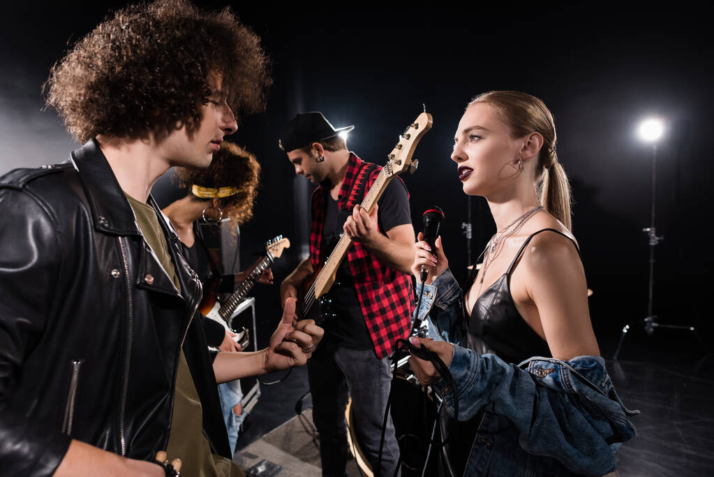 KYIV, UKRAINE - AUGUST 25, 2020: Rock band musician and blonde woman with microphone talking near guitarists with backlit on background - Photo, Image
