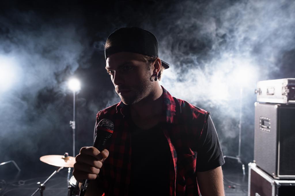 Rock band zanger met microfoon, met rook en achtergrondverlichting op wazige achtergrond - Foto, afbeelding