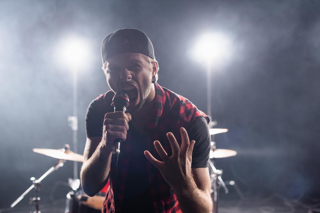 Rock grubu vokalisti mikrofonu bulanık arkaplanda tutarken çığlık atıyor - Fotoğraf, Görsel