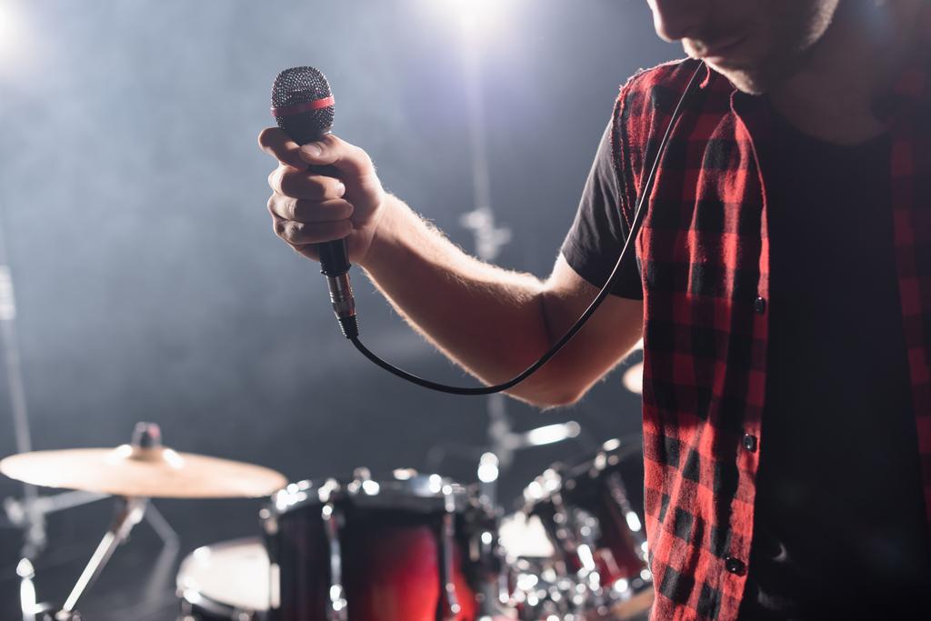 Oříznutý pohled na zpěváka s mikrofonem s rozmazaným bubnem na pozadí - Fotografie, Obrázek