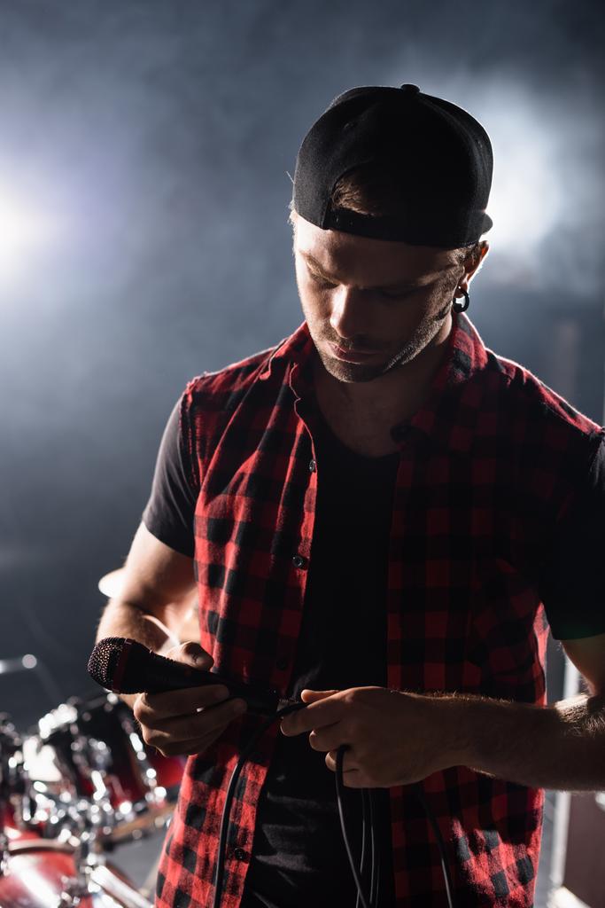Ροκ μπάντα τραγουδιστής κρατώντας μικρόφωνο και αγγίζοντας σύρμα σε θολή φόντο - Φωτογραφία, εικόνα