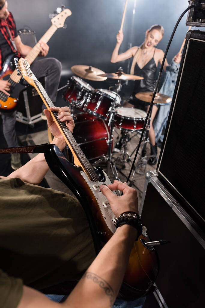 KIEW, UKRAINE - 25. AUGUST 2020: Mann mit Pickel spielt Bassgitarre neben Combo-Verstärker, blonde Frau spielt Schlagzeug und Gitarrist auf verschwommenem Hintergrund - Foto, Bild