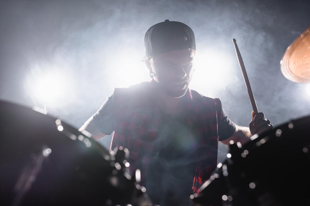 Muzyk rockowy z pałeczką perkusyjną grający na perkusji z dymem i podświetlonym na tle - Zdjęcie, obraz