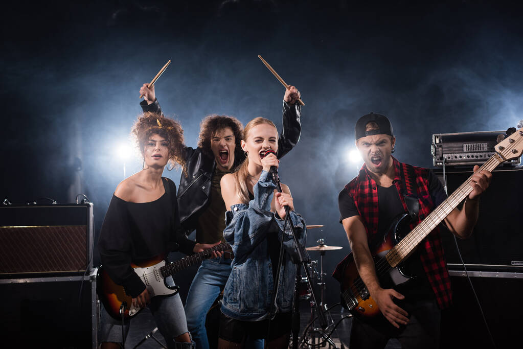 KYIV, UCRANIA - 25 de agosto de 2020: Músicos de bandas de rock gritando mientras sostienen instrumentos musicales con retroiluminación en negro - Foto, Imagen