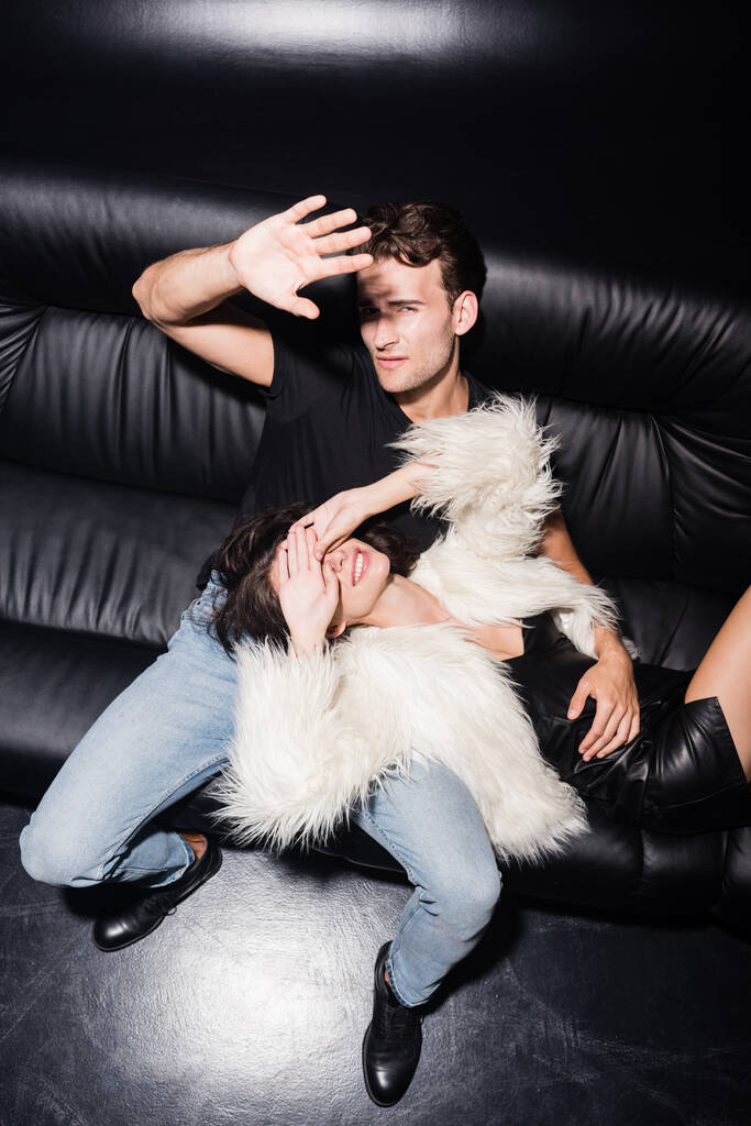 Magas látószögű kilátás szexi pár csukott szemmel és arccal a kezét, miközben ül a kanapén a nightclub - Fotó, kép