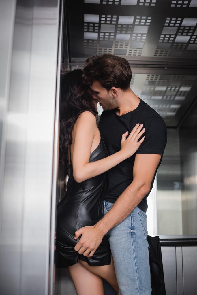 Mann in schwarzem T-Shirt und Jeans berührt Gesäß lockiger Frau im Fahrstuhl - Foto, Bild