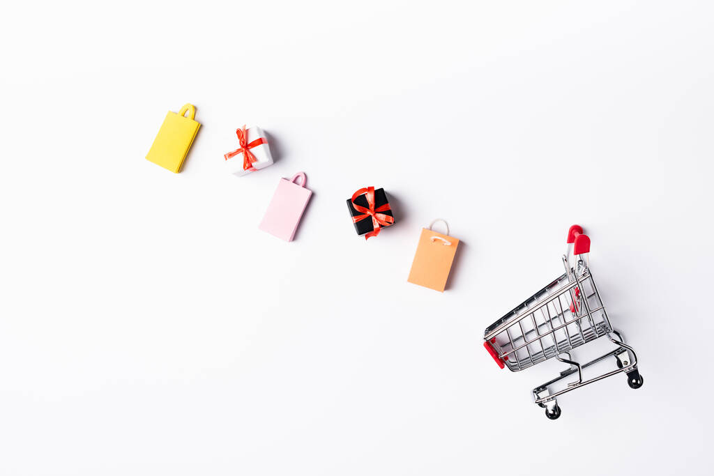 Top view of colorful toy shopping bags and gift boxes near cart on white background - Photo, Image