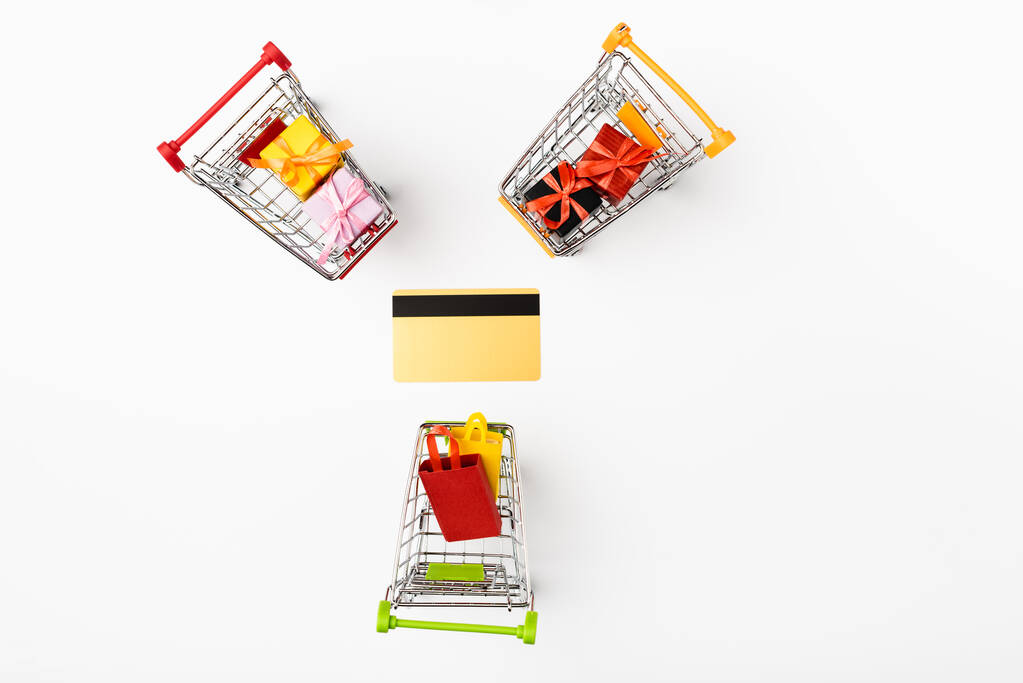 Vue du dessus des chariots d'achat de jouets avec des cadeaux et des sacs près de la carte de crédit sur fond blanc - Photo, image