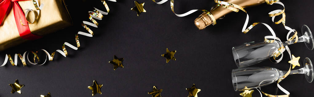Cultivo horizontal de botella de champán, copas y regalo cerca de la decoración sobre fondo negro  - Foto, imagen