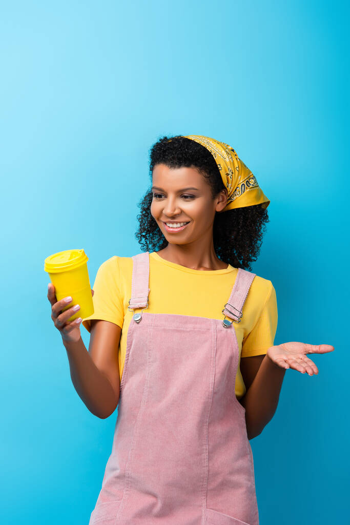 mujer afroamericana feliz sosteniendo taza reutilizable en azul - Foto, Imagen