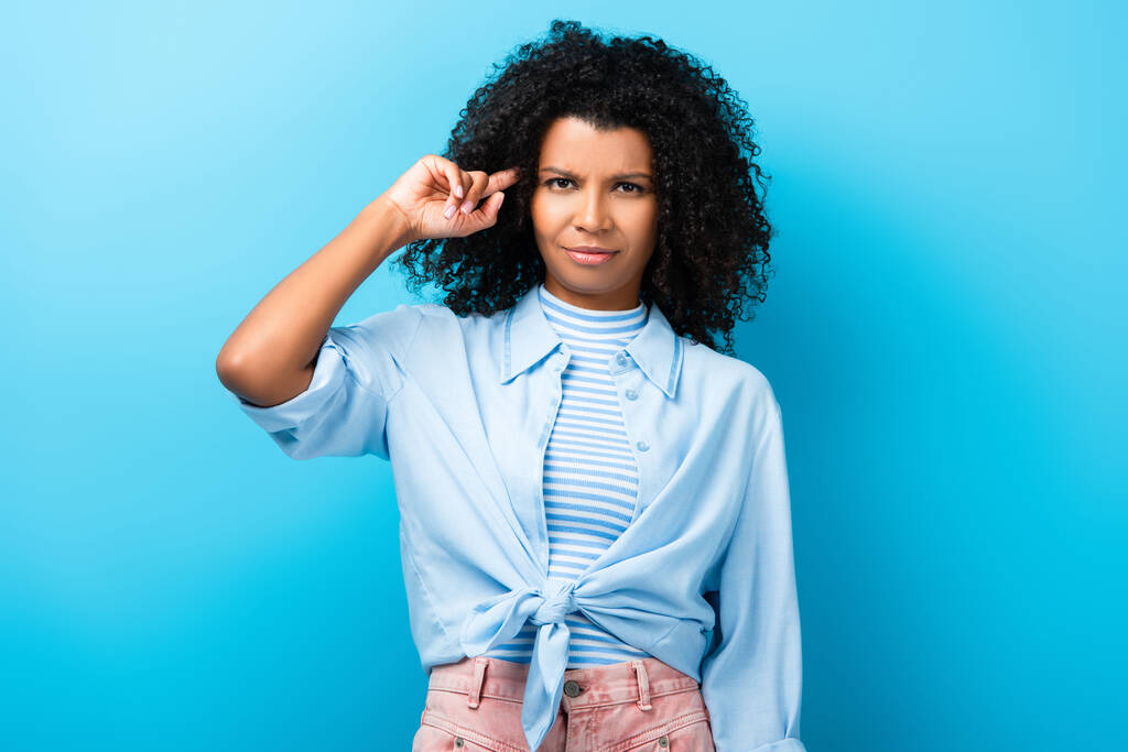 mujer afroamericana disgustado señalando con el dedo en la cabeza en azul - Foto, imagen