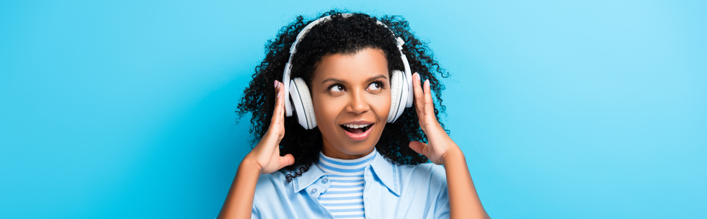 animado afro-americano mulher ouvindo música em fones de ouvido em azul, banner - Foto, Imagem
