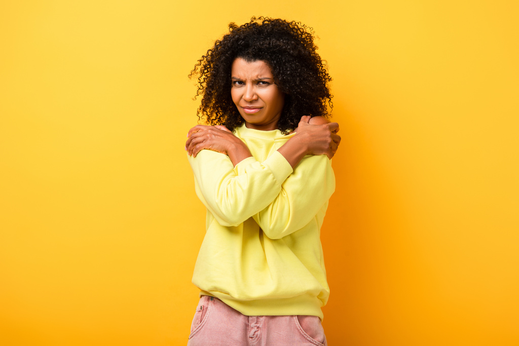 displeased african american woman embracing herself on yellow - Photo, Image