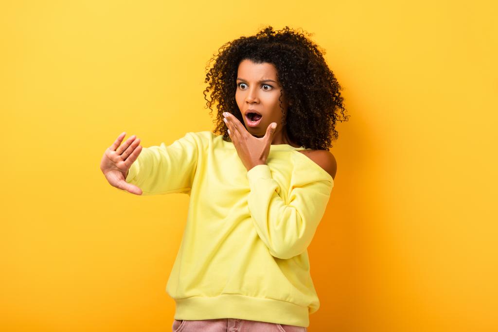 chocado afro-americano mulher olhando para unhas em amarelo - Foto, Imagem