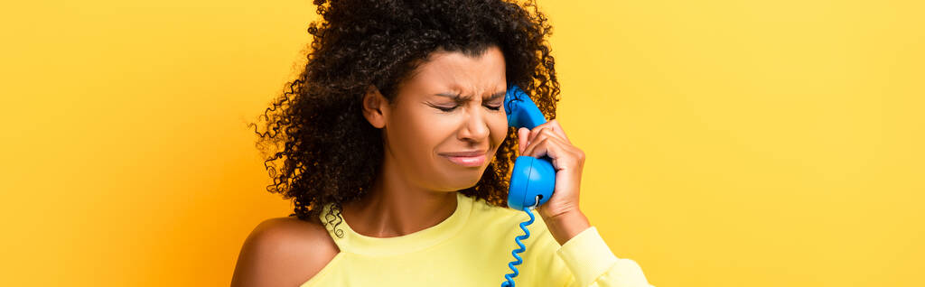 Αναστατωμένη Αφροαμερικανή γυναίκα που μιλάει στο vintage τηλέφωνο στο κίτρινο, banner - Φωτογραφία, εικόνα