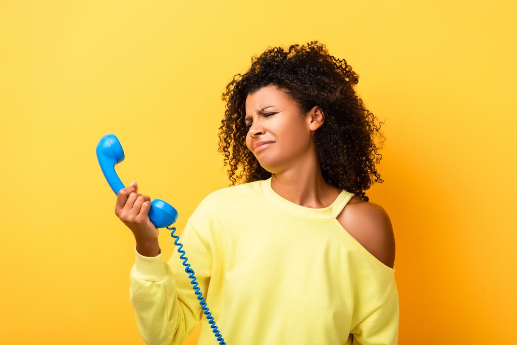 засмучена афро - американська жінка, яка дивиться на старовинний телефон по жовтому. - Фото, зображення