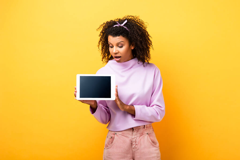 schockierte Afroamerikanerin hält digitales Tablet mit leerem Bildschirm auf gelb  - Foto, Bild