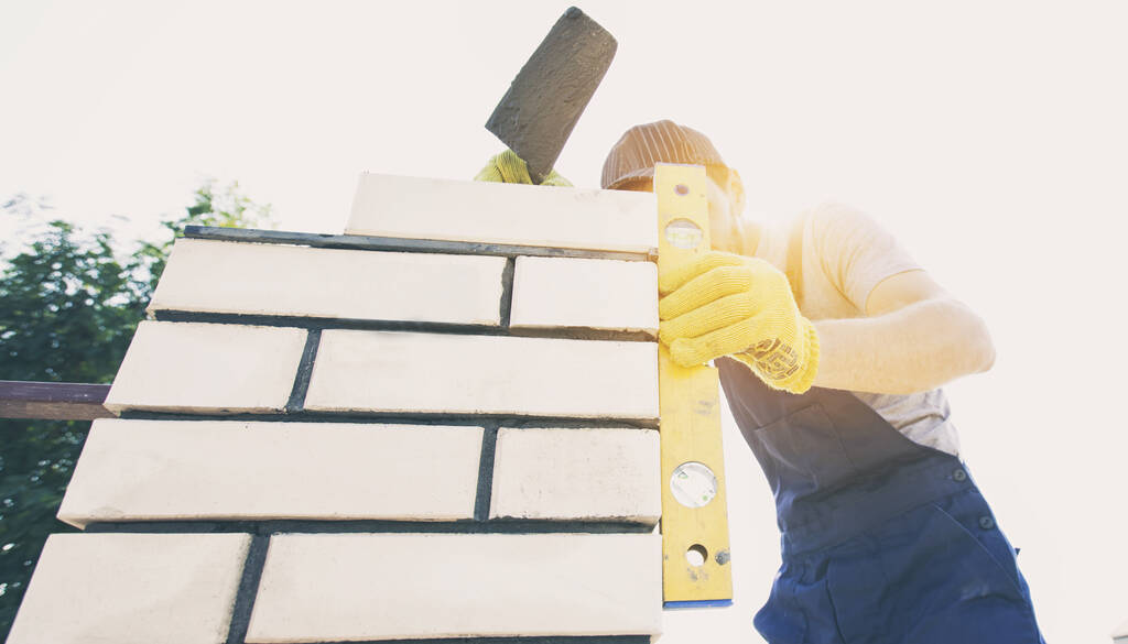 Een arbeider bouwt een hekpaal van bakstenen - Foto, afbeelding