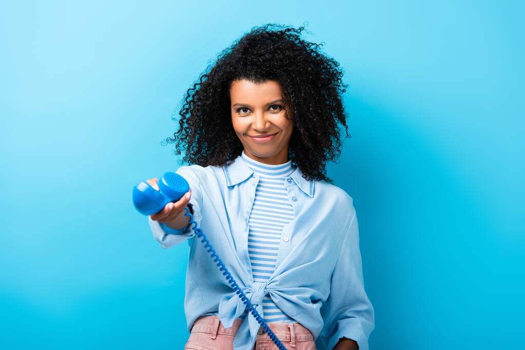 pleased african american woman holding retro telephone on blue - Photo, Image