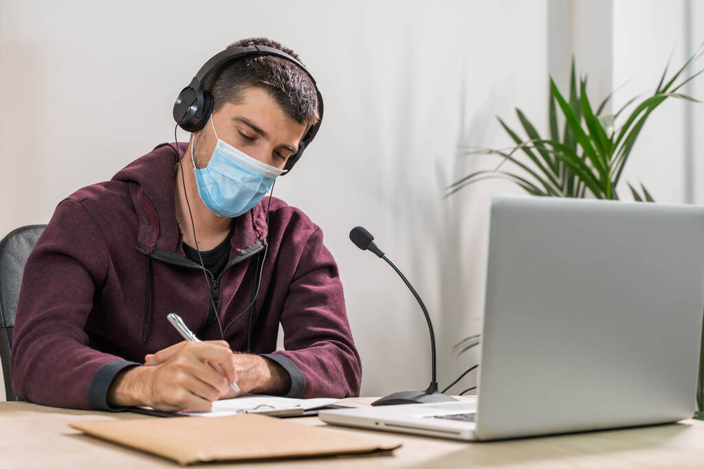 Telemarketeer man werkt aan laptop en praat op een headset met gezichtsmasker op kantoor. Zelf geïsoleerd en thuis werkend door het coronavirus. Zakelijke werknemer antwoord klanten oproepen.  - Foto, afbeelding