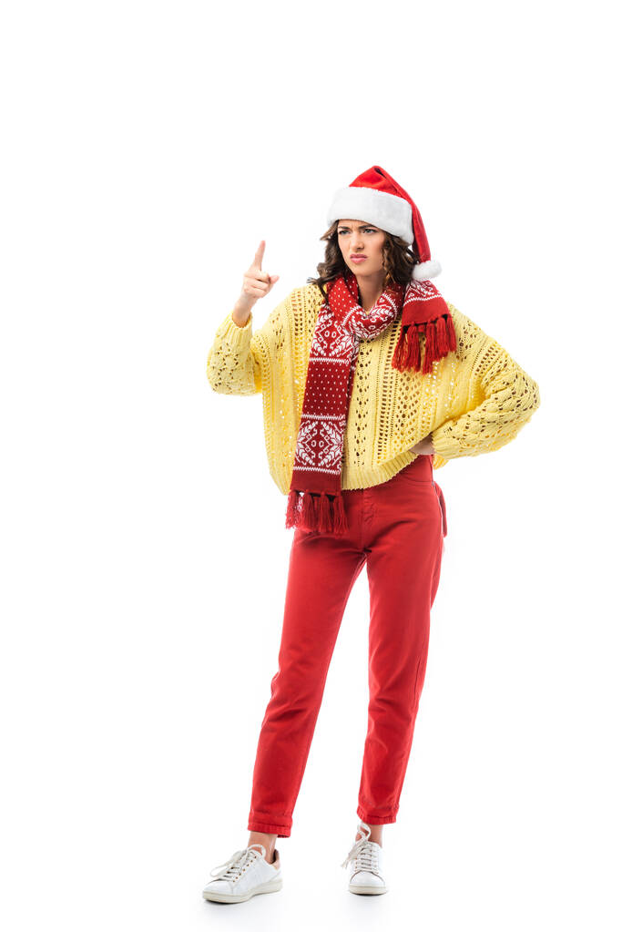 unzufriedene Frau mit Weihnachtsmütze und Schal, die mit der Hand auf der Hüfte steht und mit dem Finger auf weiß zeigt  - Foto, Bild