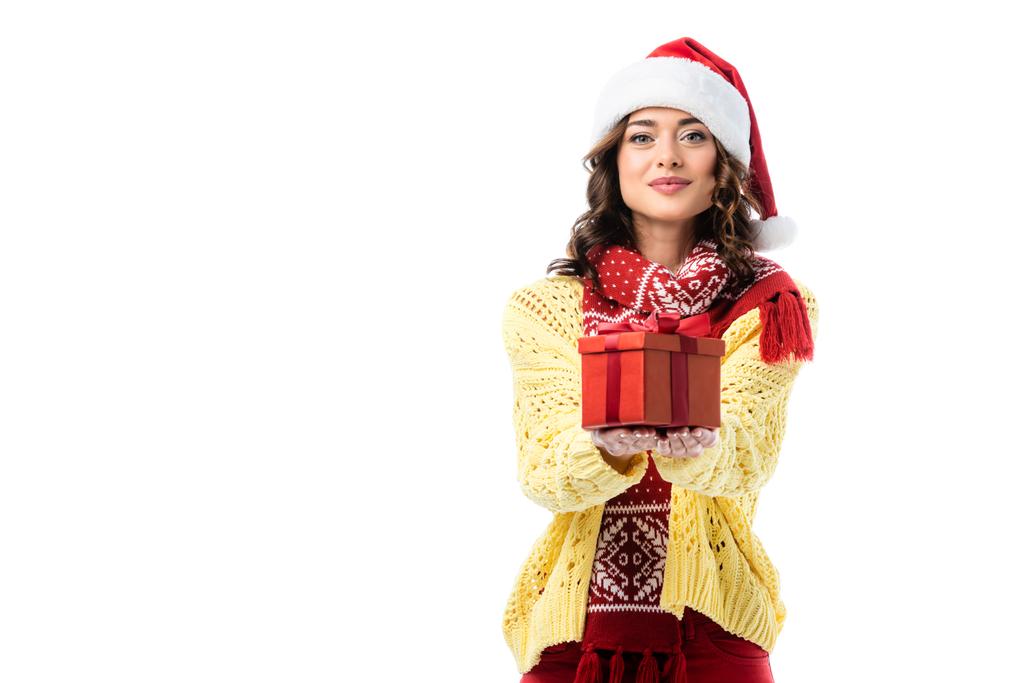 задоволена жінка в капелюсі Санта і червоний шарф тримає подарунок ізольовано на білому
 - Фото, зображення