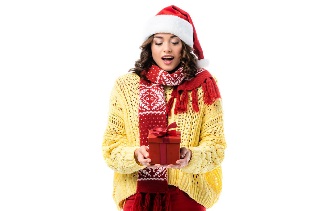 excited woman in santa hat and red scarf looking at present isolated on white - Photo, Image