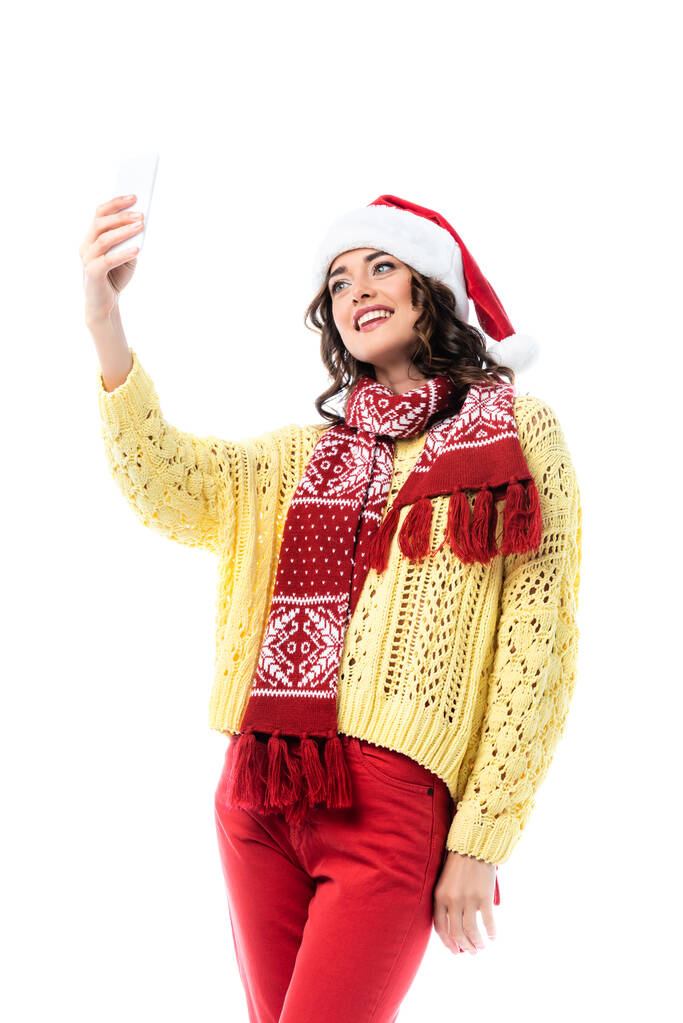 tevreden vrouw in santa hoed en sjaal het nemen van selfie op smartphone geïsoleerd op wit  - Foto, afbeelding
