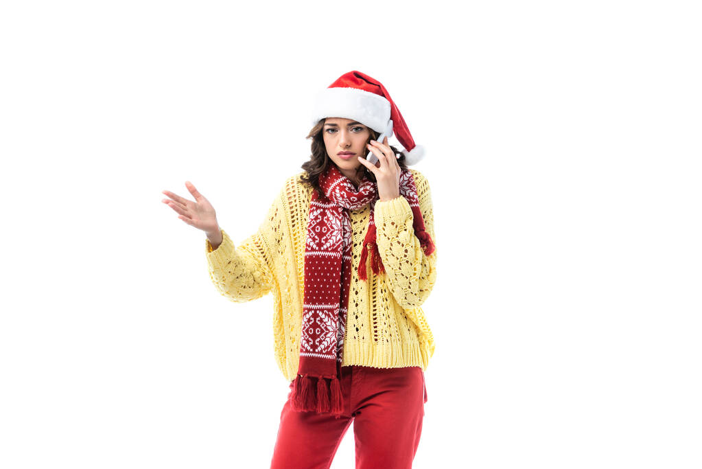 giovane donna in cappello di Babbo Natale e sciarpa parlando su smartphone e gesticolando isolata su bianco  - Foto, immagini